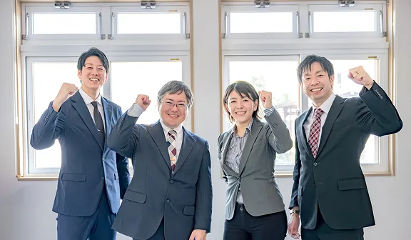 オフィスの窓を背景にガッツポーズをする社員4人